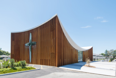 Pictured on a sunny day the building, clad completely in natural cedar, features a dominating concave roofline.